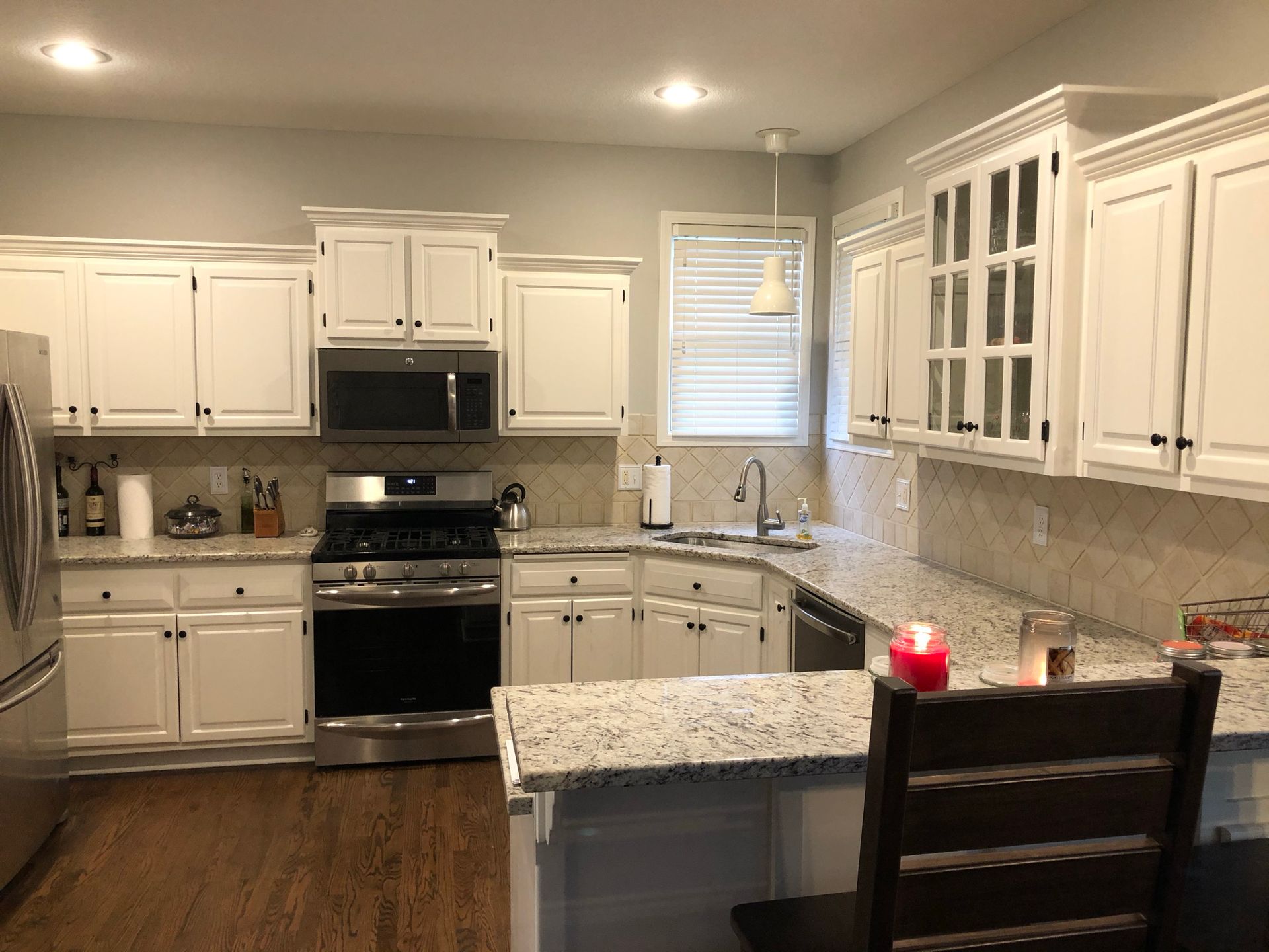 A kitchen with white cabinets , granite counter tops , stainless steel appliances and a candle on the counter.