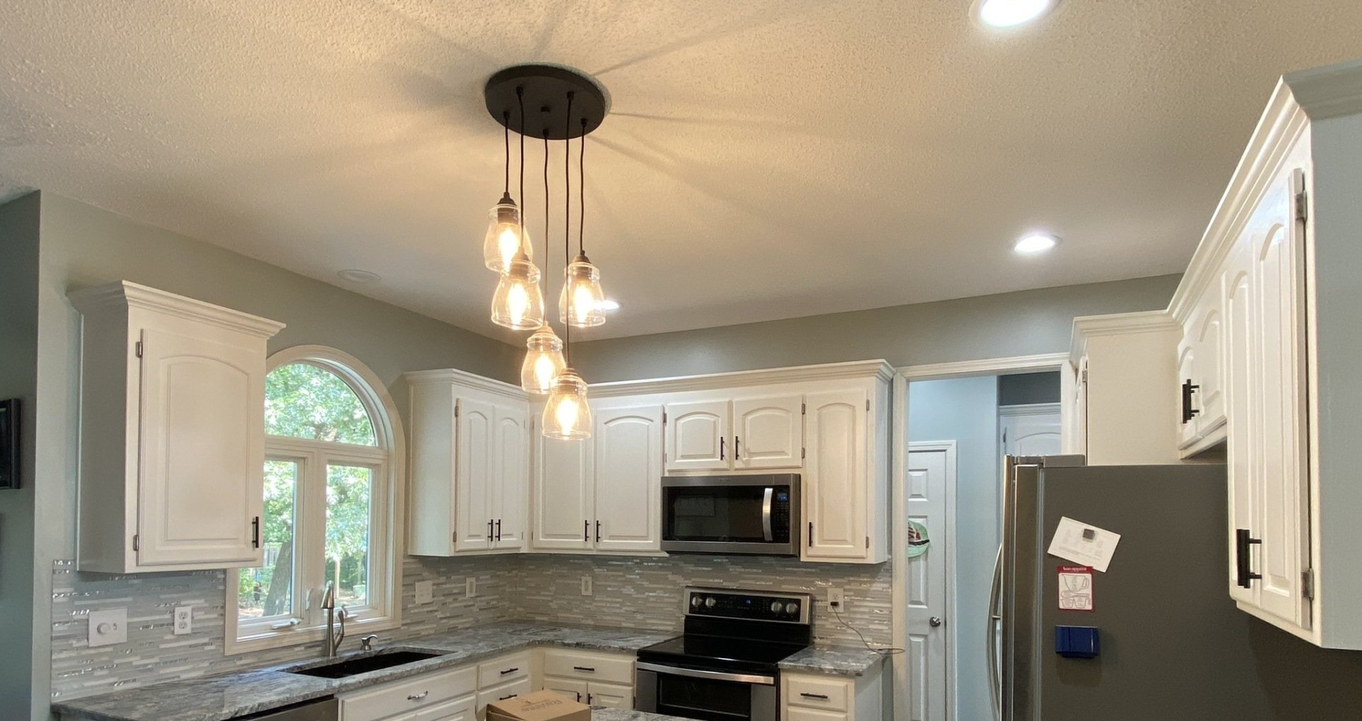 A kitchen with white cabinets , stainless steel appliances , granite counter tops and a pendant light.