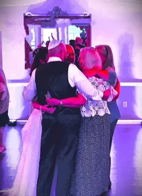 A bride and groom are dancing with their parents at a wedding reception.