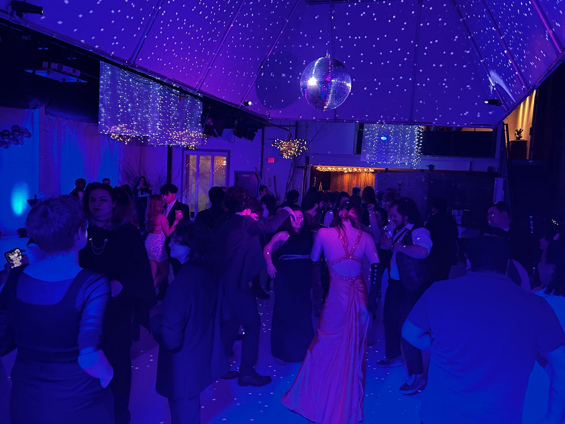 a large group of people are dancing in a room with purple lights .