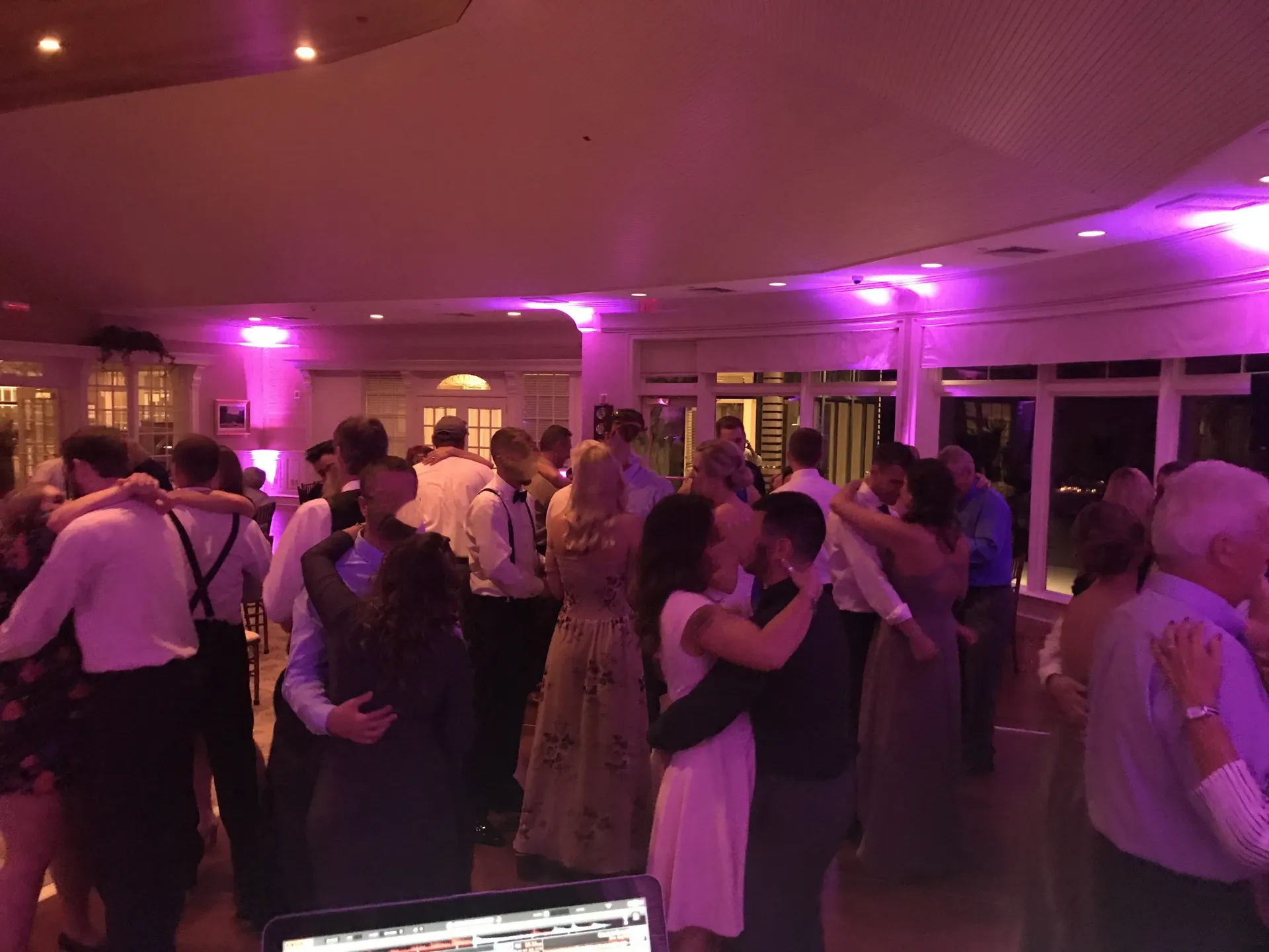 a large group of people are dancing in a room with purple lights .