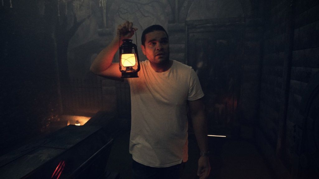A man is holding a lantern in a dark escape room.