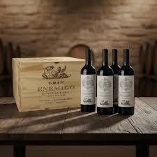 Una botella de vino sobre una mesa de madera con un sofá de cuero capitoné y persianas al fondo.