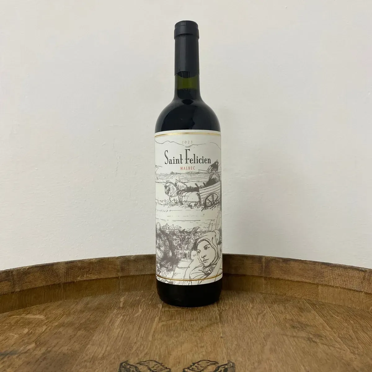 Seis botellas de vino oscuro con etiquetas color crema dispuestas sobre una mesa de madera en una habitación luminosa.