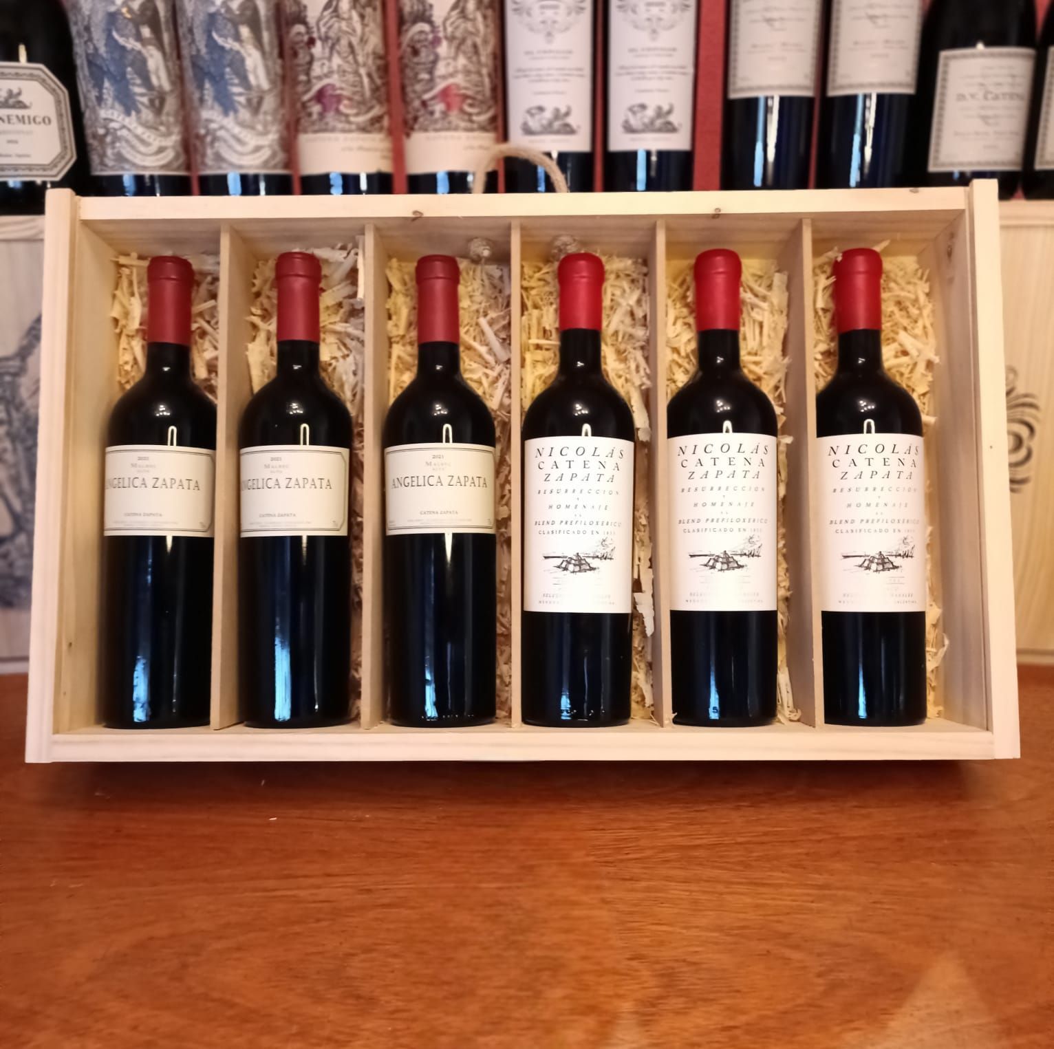 Caja de madera para vino con seis botellas de vino tinto sobre una mesa de madera.