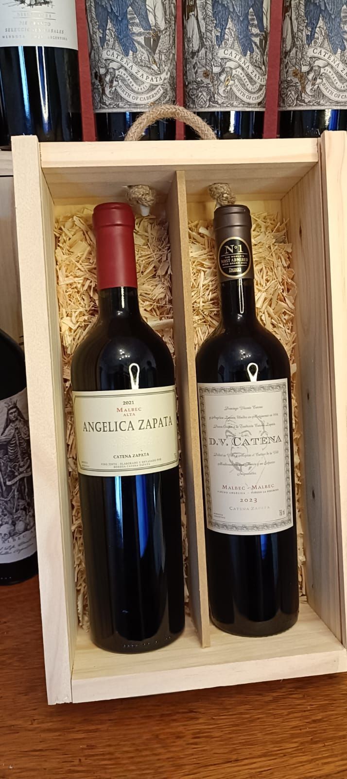 Dos botellas de vino en una caja de regalo de madera con relleno de paja y etiquetas hacia adelante.