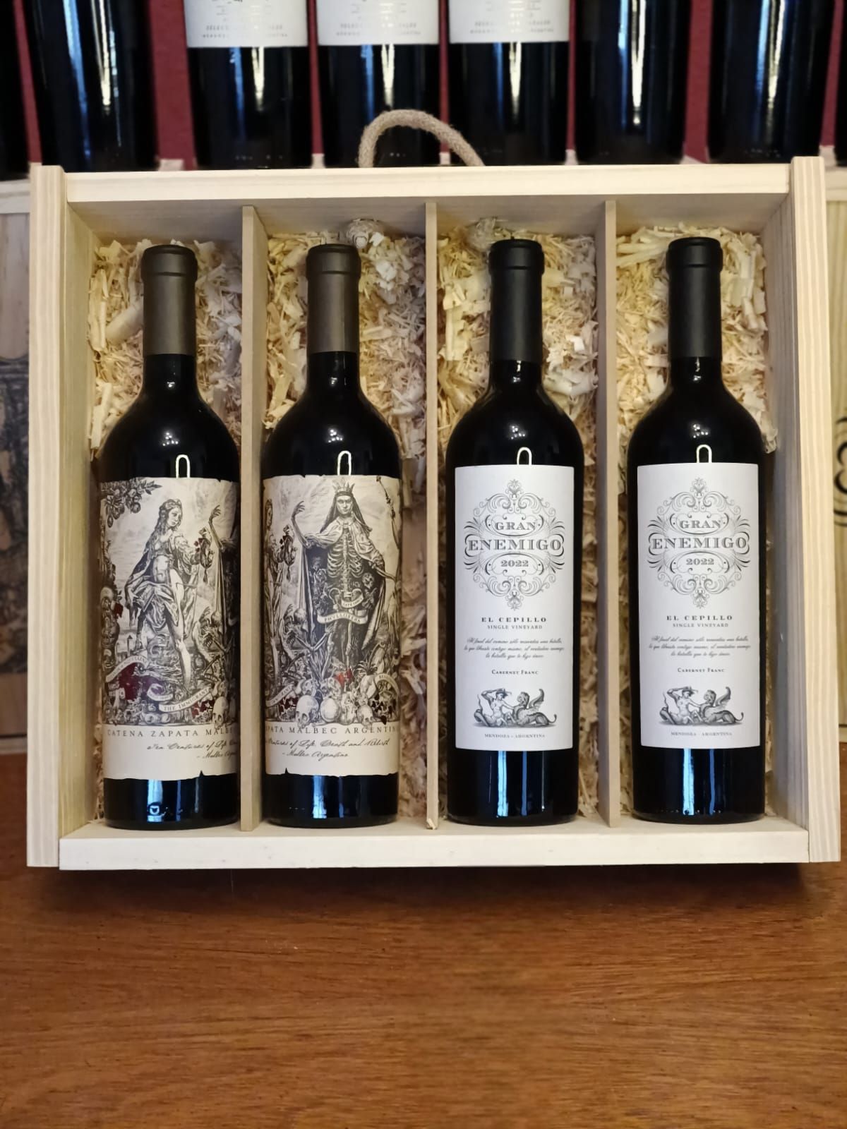 Cuatro botellas de vino en una caja de regalo de madera sobre una mesa, con etiquetas decorativas.