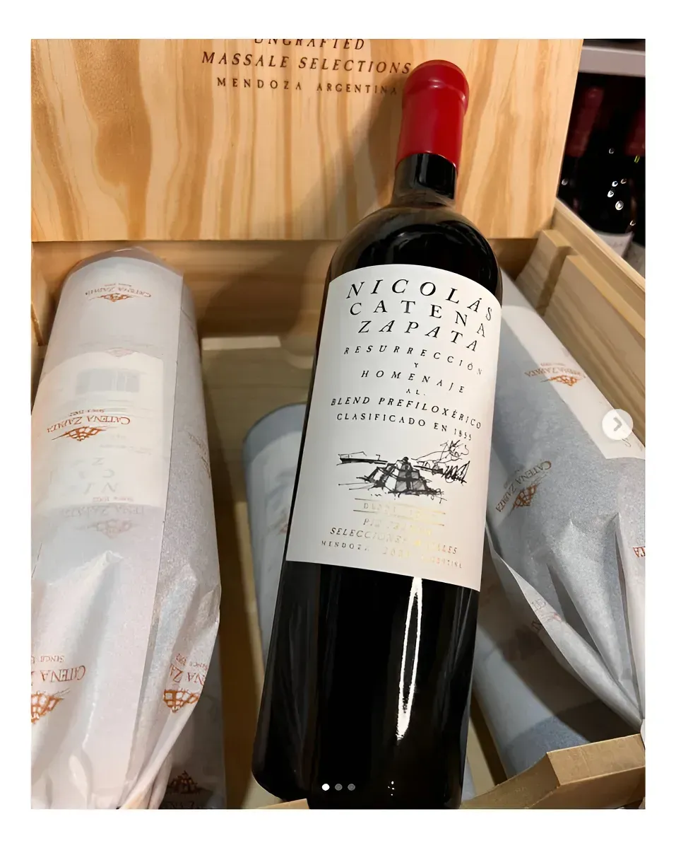 Botella de vino en una caja de regalo de madera, flanqueada por artículos envueltos en papel blanco y gris.