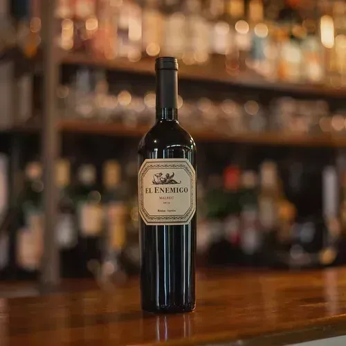 Botella de vino tinto sobre una barra de madera con botellas de licor borrosas al fondo.
