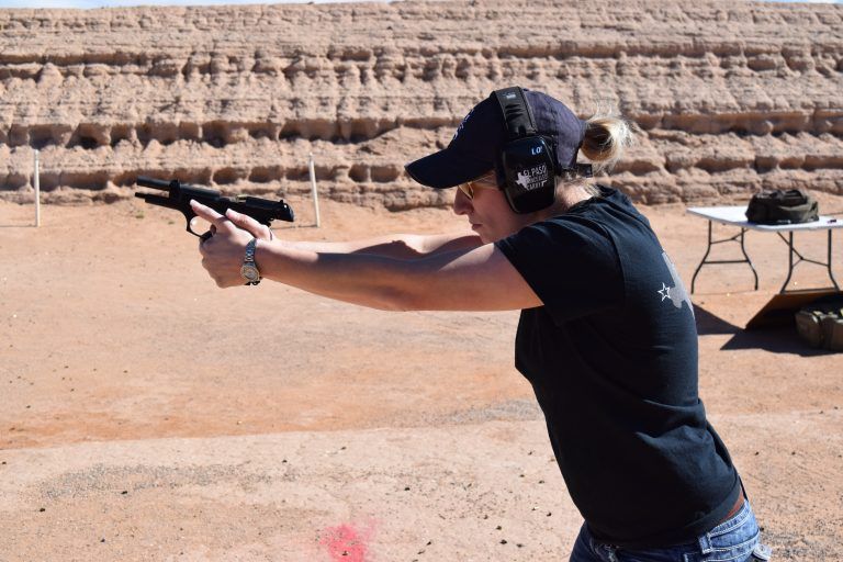 Woman shooting a handgun at an outdoor shooting range, aiming at targets.