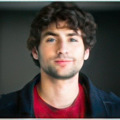 A man with curly hair and a beard is wearing a red shirt and a blue jacket.