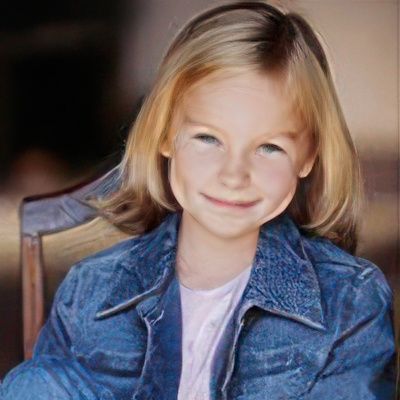 A little girl is sitting in a chair wearing a denim jacket and smiling.