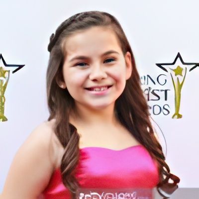 A young girl in a pink dress is smiling in front of a king awards sign