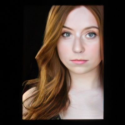 A woman with long red hair and blue eyes looks at the camera