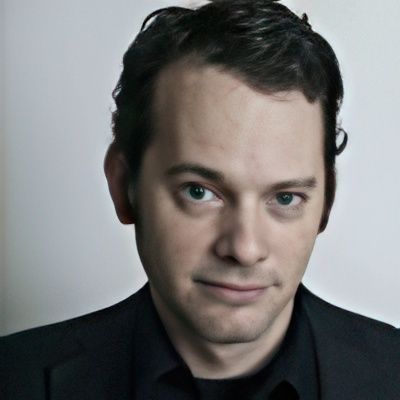 A man in a suit and black shirt looks at the camera