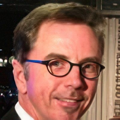 A man wearing glasses and a tuxedo smiles for the camera