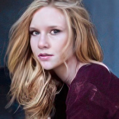 A woman with long blonde hair is wearing a purple sweater