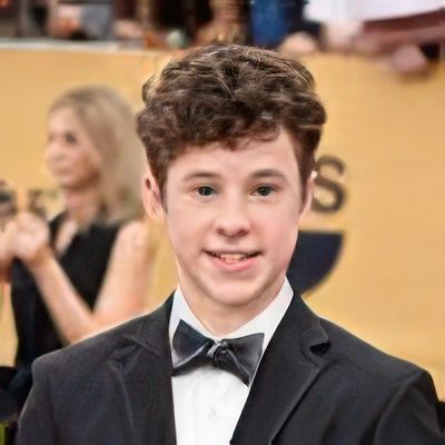 A young man in a suit and bow tie is standing on a red carpet.