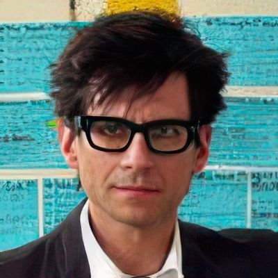 A man wearing glasses and a suit looks at the camera