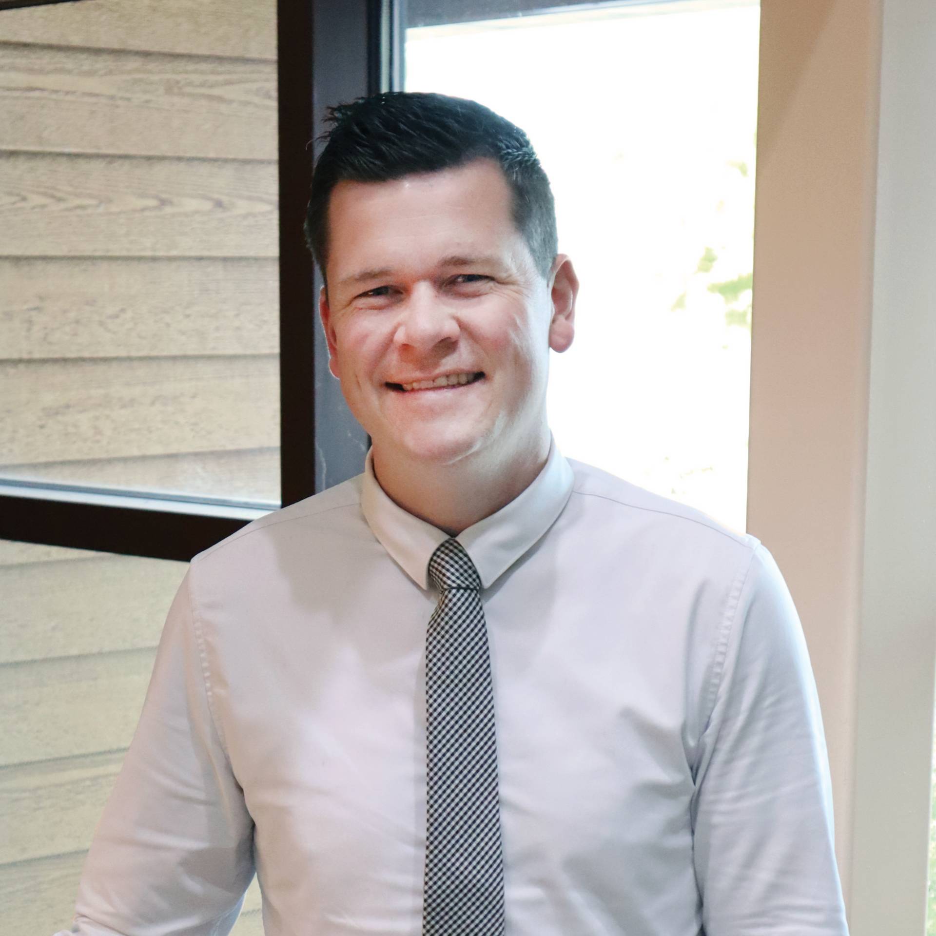 Man in light blue shirt and patterned tie smiling at the camera, inside a building.