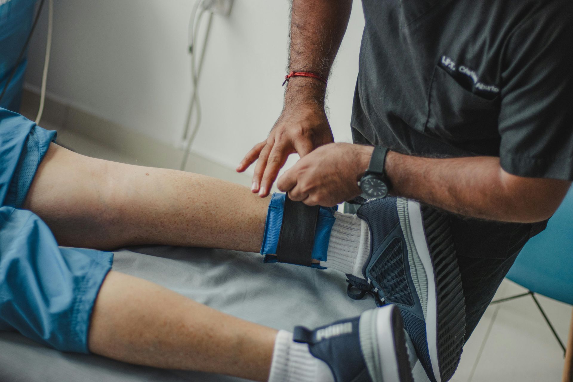 Person's leg with a compression wrap being applied by someone. Indoors, medical setting.