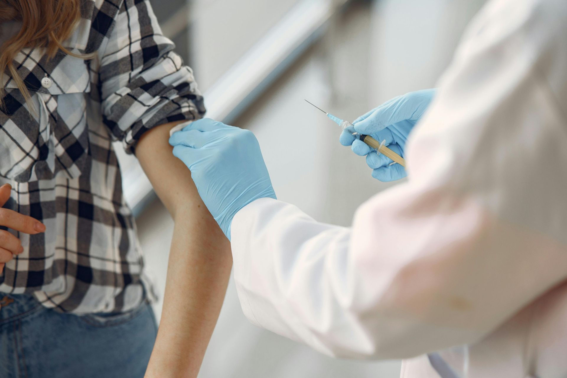 Person receiving a vaccination shot in the arm; doctor holding syringe with blue gloves.