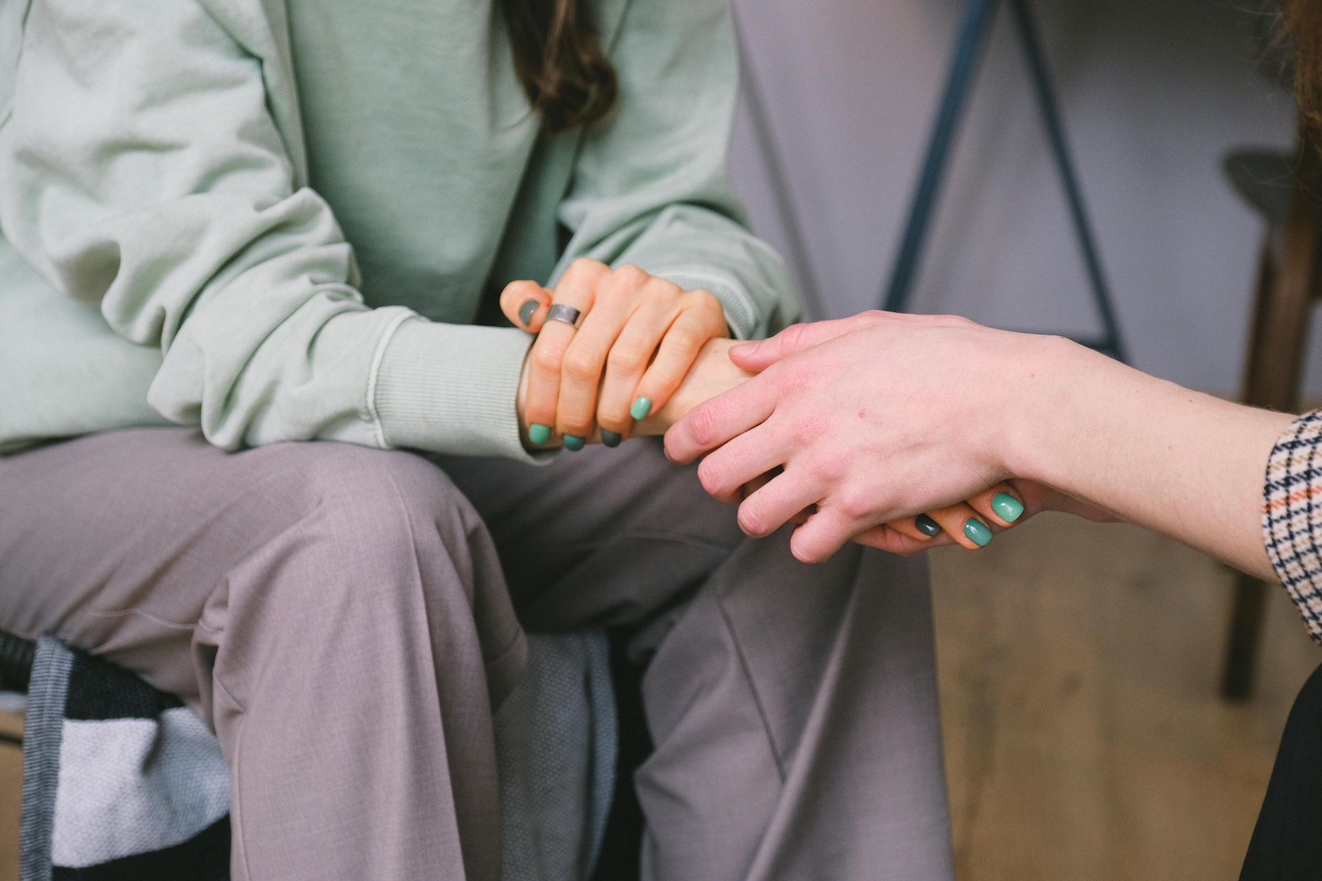 Person holding hands with another, offering comfort. Teal nails, neutral clothing.