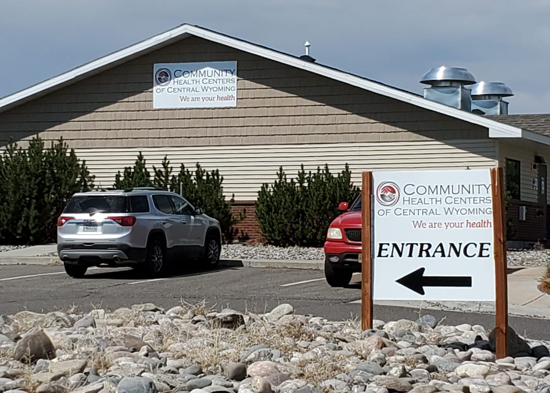 Community Health Center building with cars in the parking area, entrance sign.