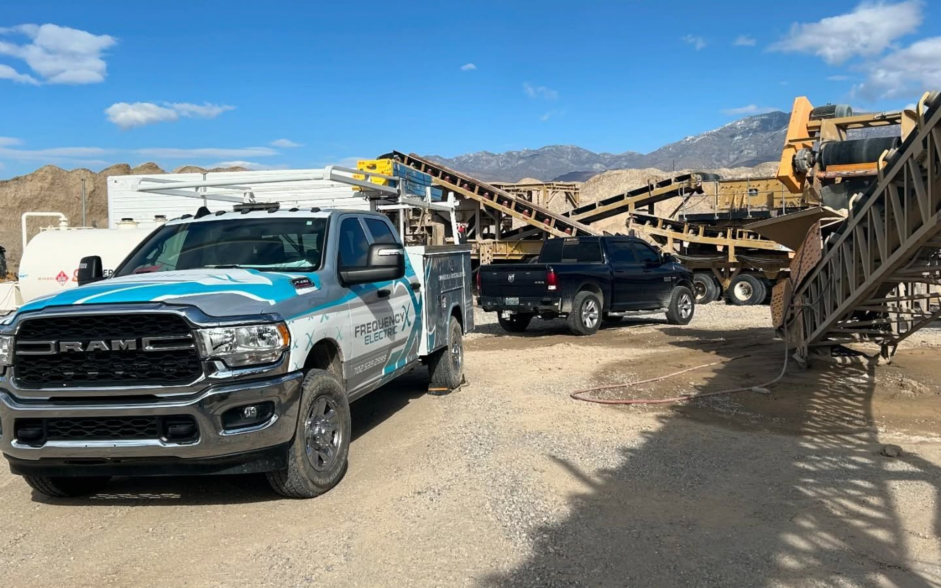 RAM work truck parked at a gravel pit with machinery and mountains in the background.