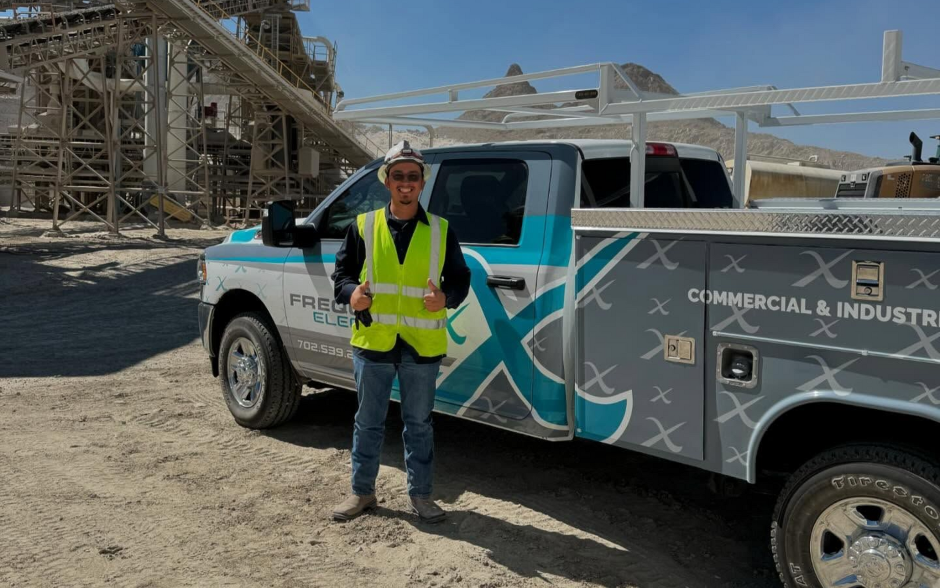 Man in safety vest and hard hat stands next to a work truck with the company logo 
