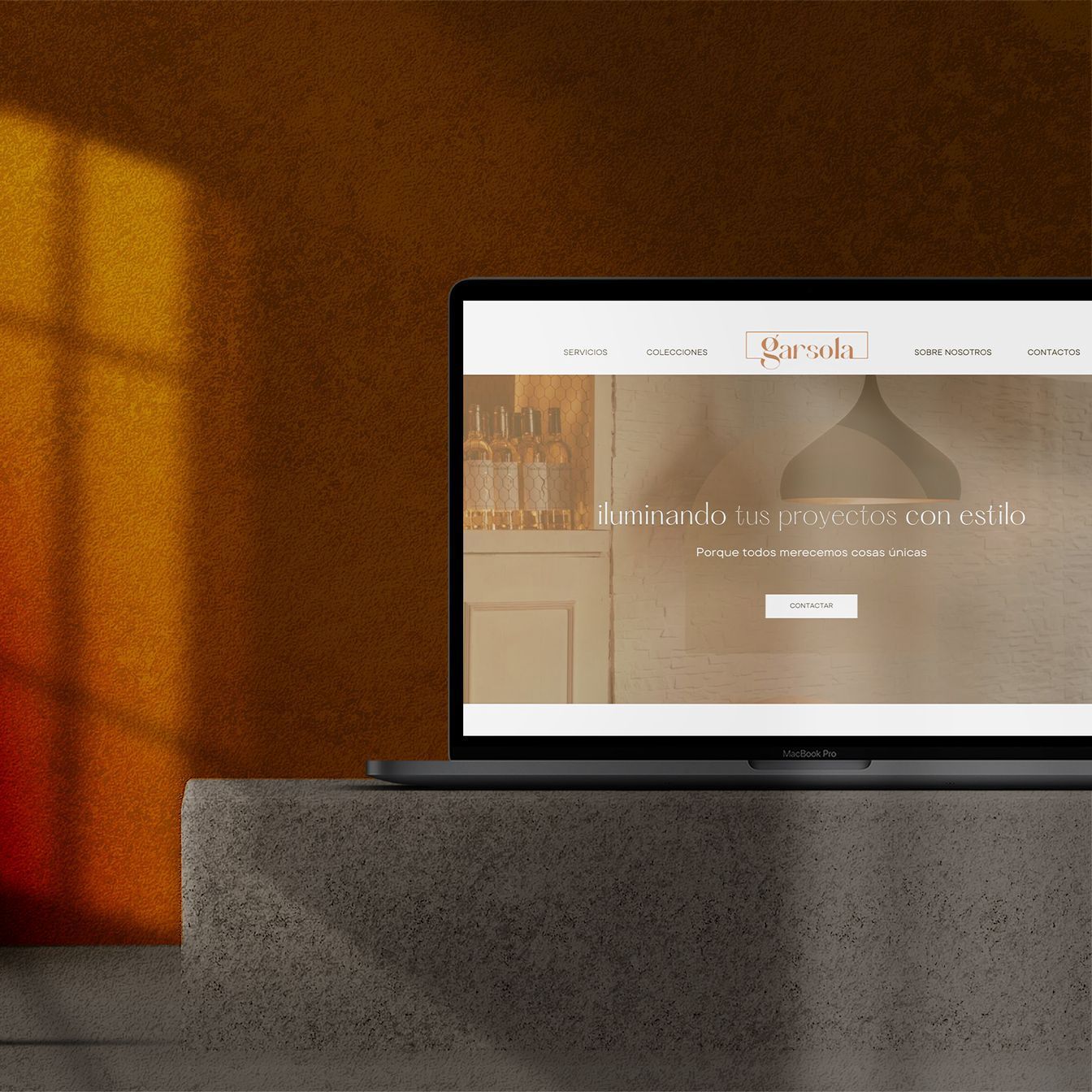 Un ordenador portátil muestra una página web sobre un pedestal de piedra, frente a una pared de color naranja cálido iluminada por la luz de una ventana.