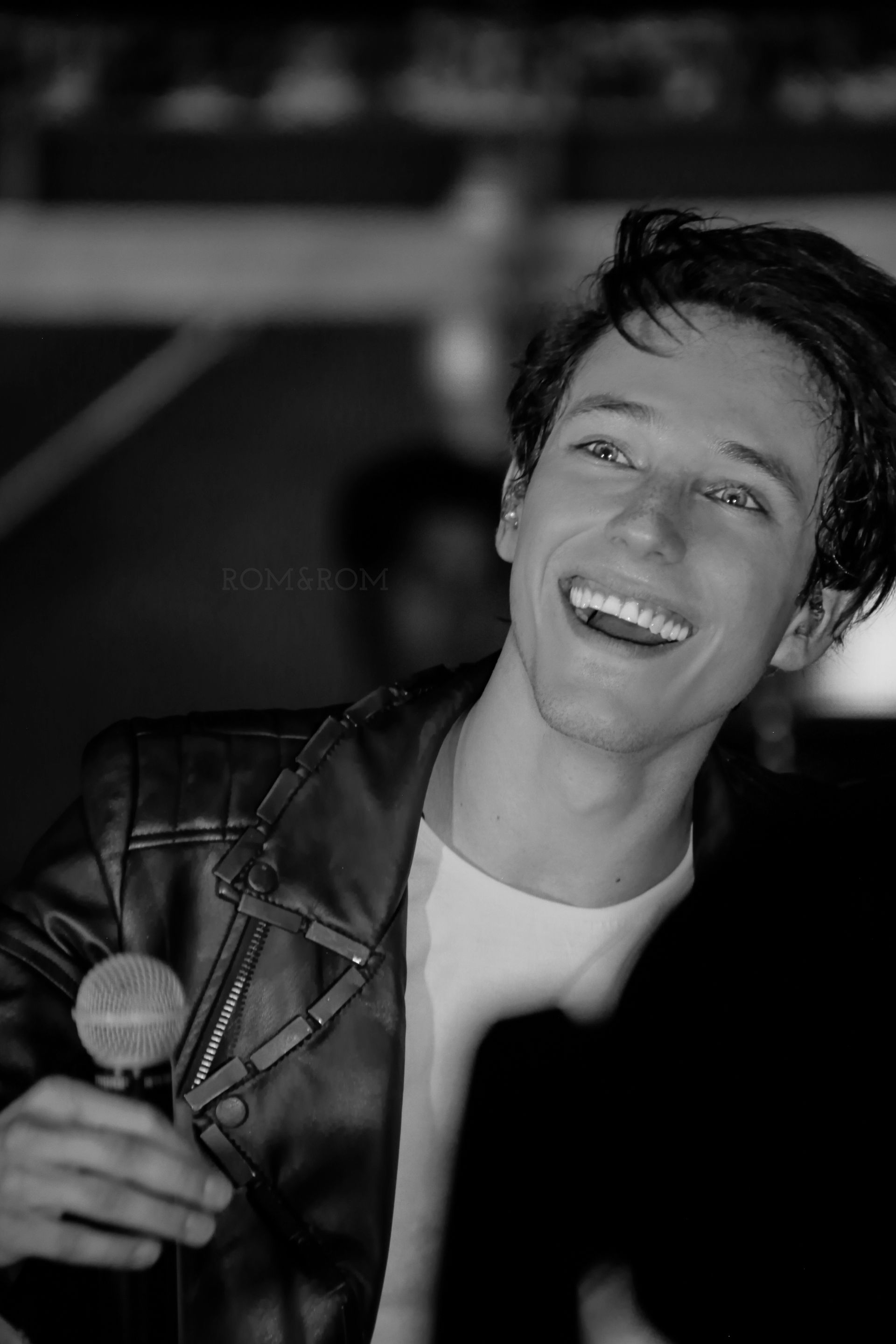 Retrato en blanco y negro de una cantante sonriente sosteniendo un micrófono en el escenario.