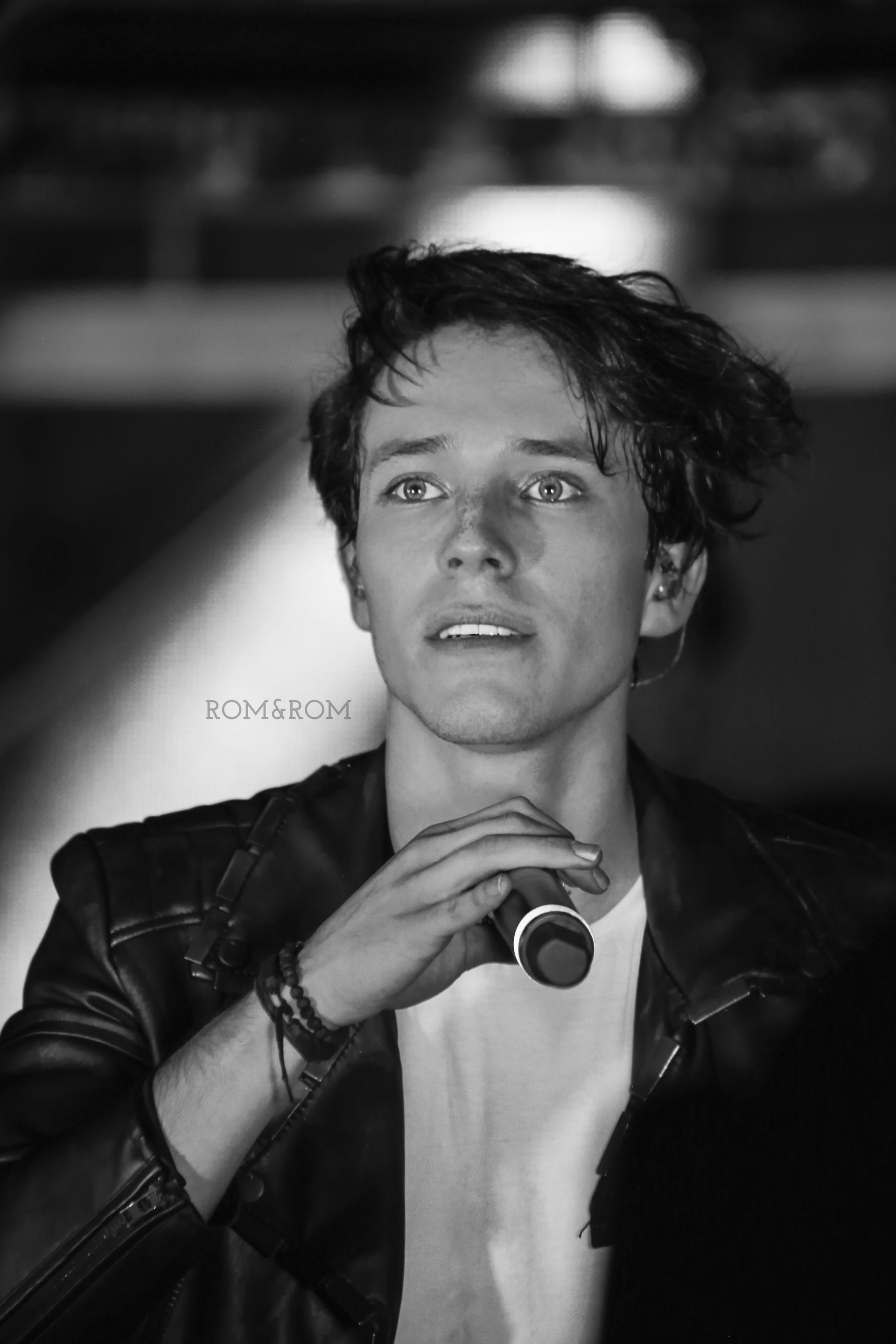 Retrato en blanco y negro de una persona sosteniendo un micrófono, mirando hacia arriba en un escenario.