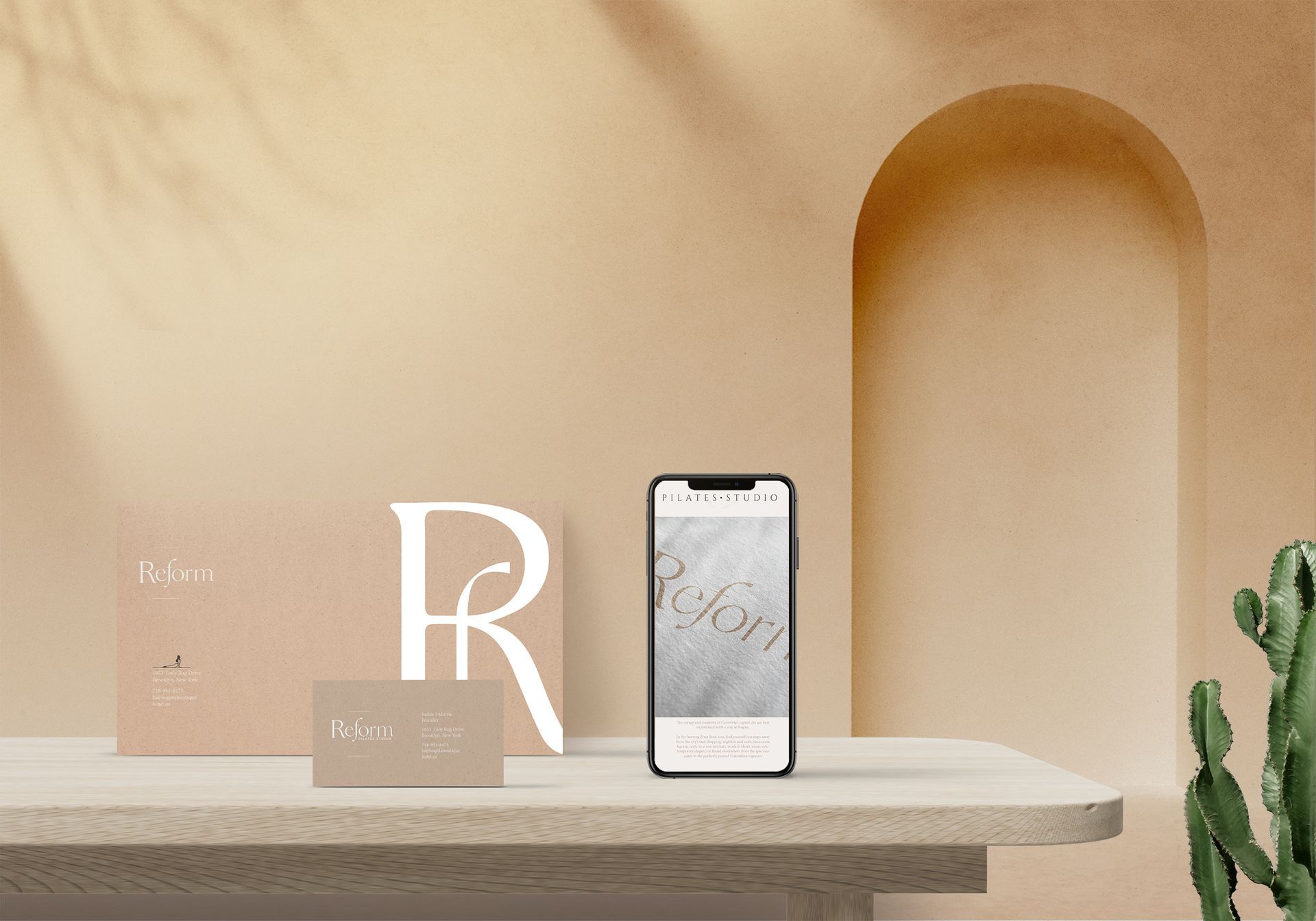 Estantería minimalista de color beige con un teléfono inteligente, decoración con la letra R y un pequeño cactus.