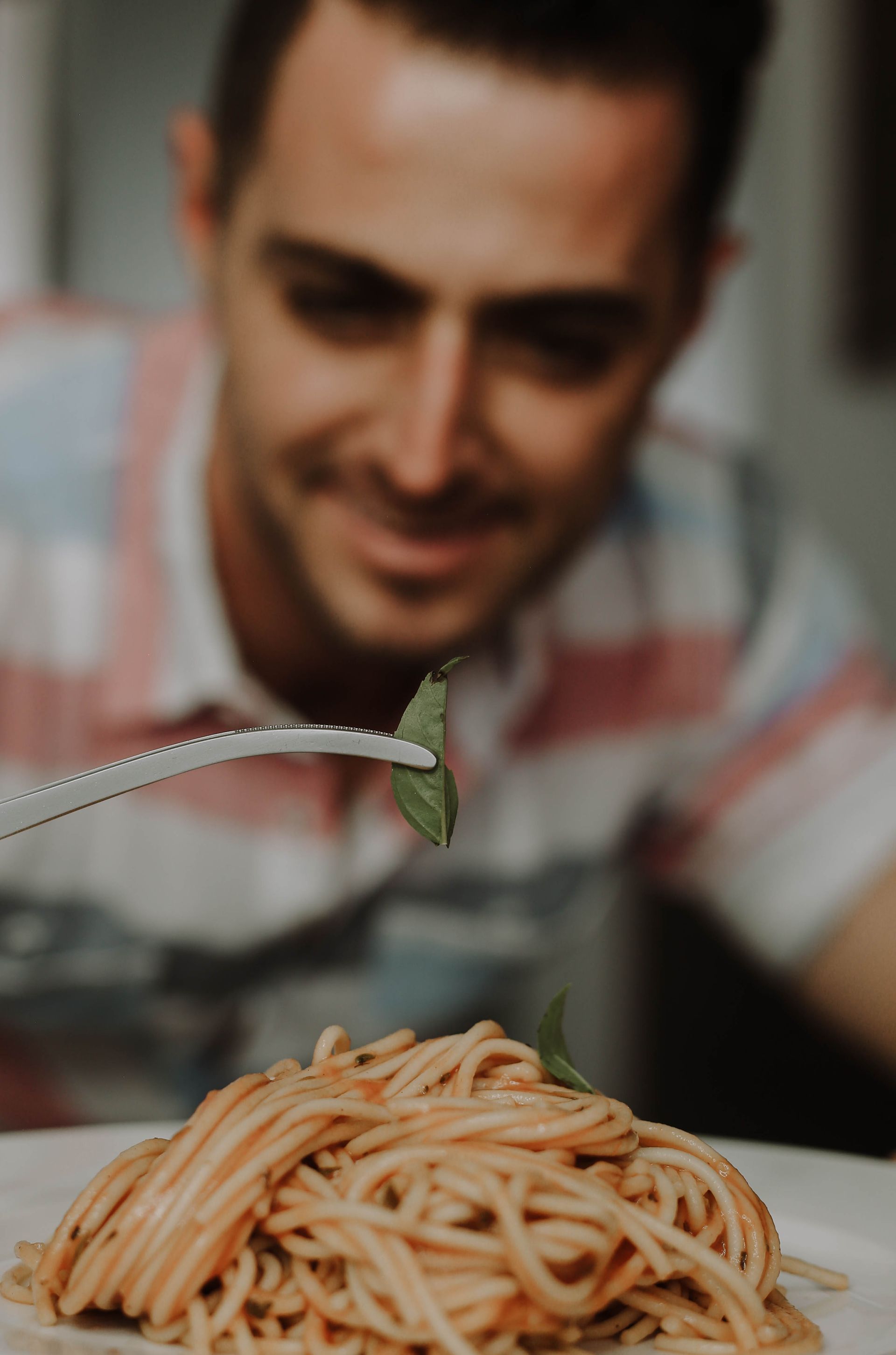 Persona levantando espaguetis con un tenedor sobre un plato de pasta, con el fondo borroso.