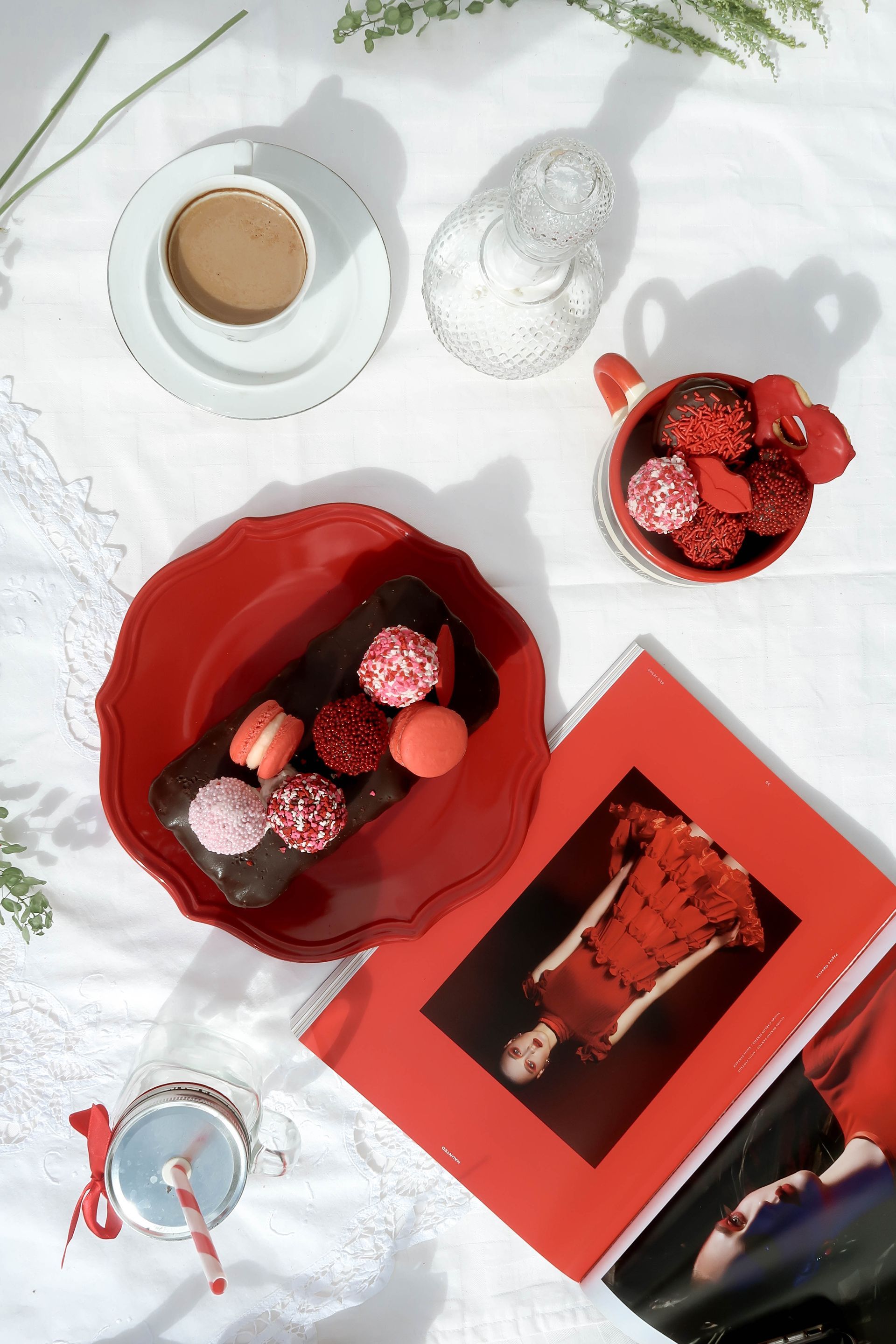 Caja de regalo roja para postres con fresas y bombones junto a una taza de café sobre un mantel blanco.