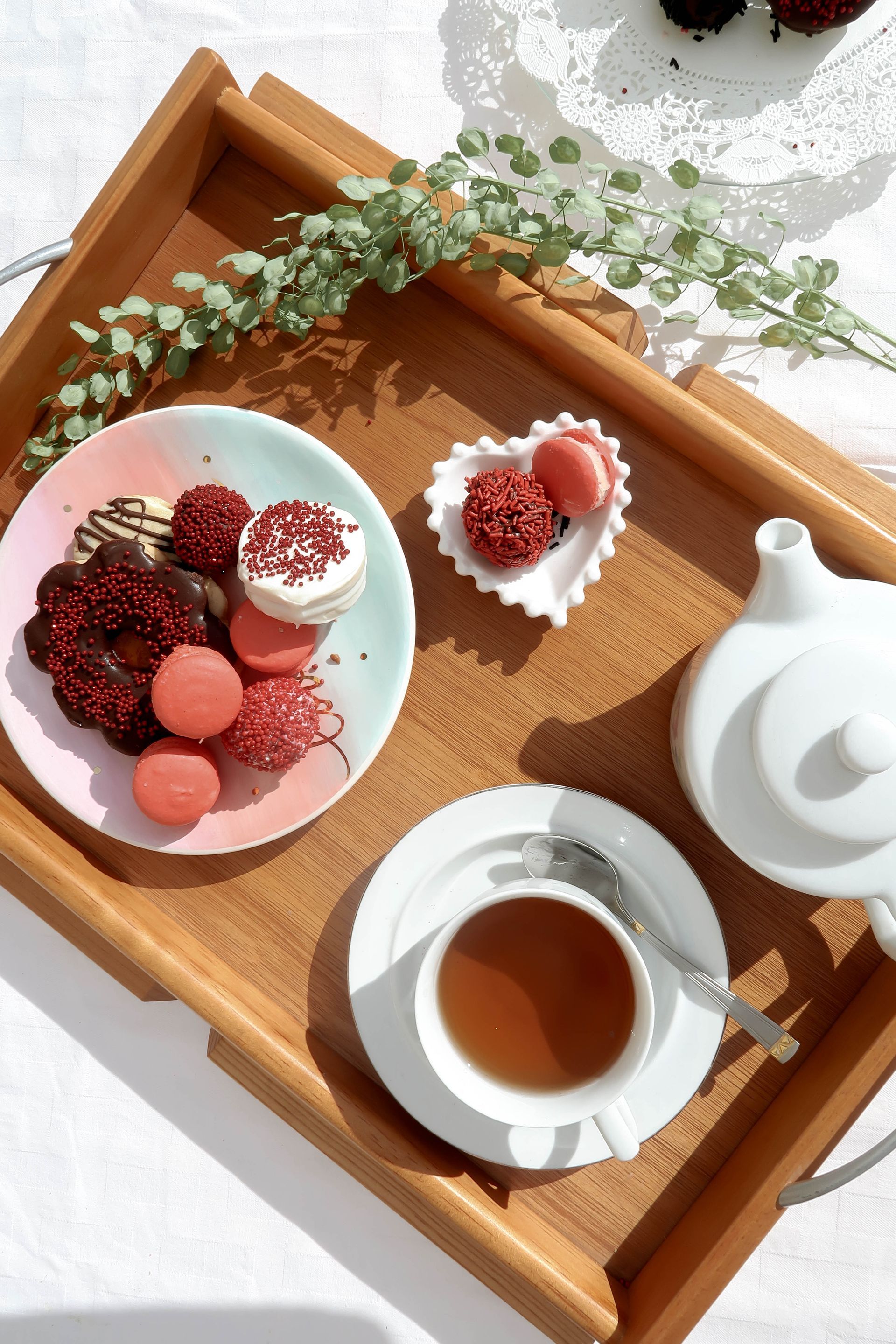 Juego de té con bayas en una bandeja de madera, una tetera blanca y una taza de té sobre una mesa cubierta de encaje.