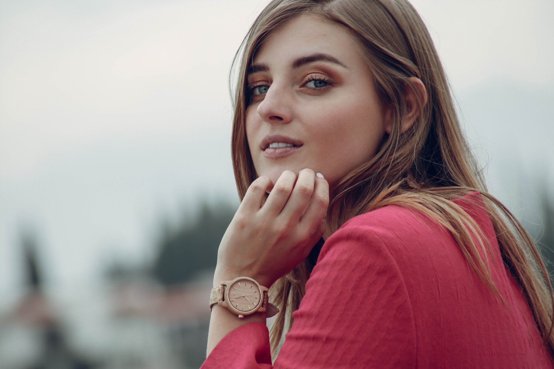 Mujer con un suéter rosa posando al aire libre, apoyando la barbilla en la mano y mirando a la cámara.