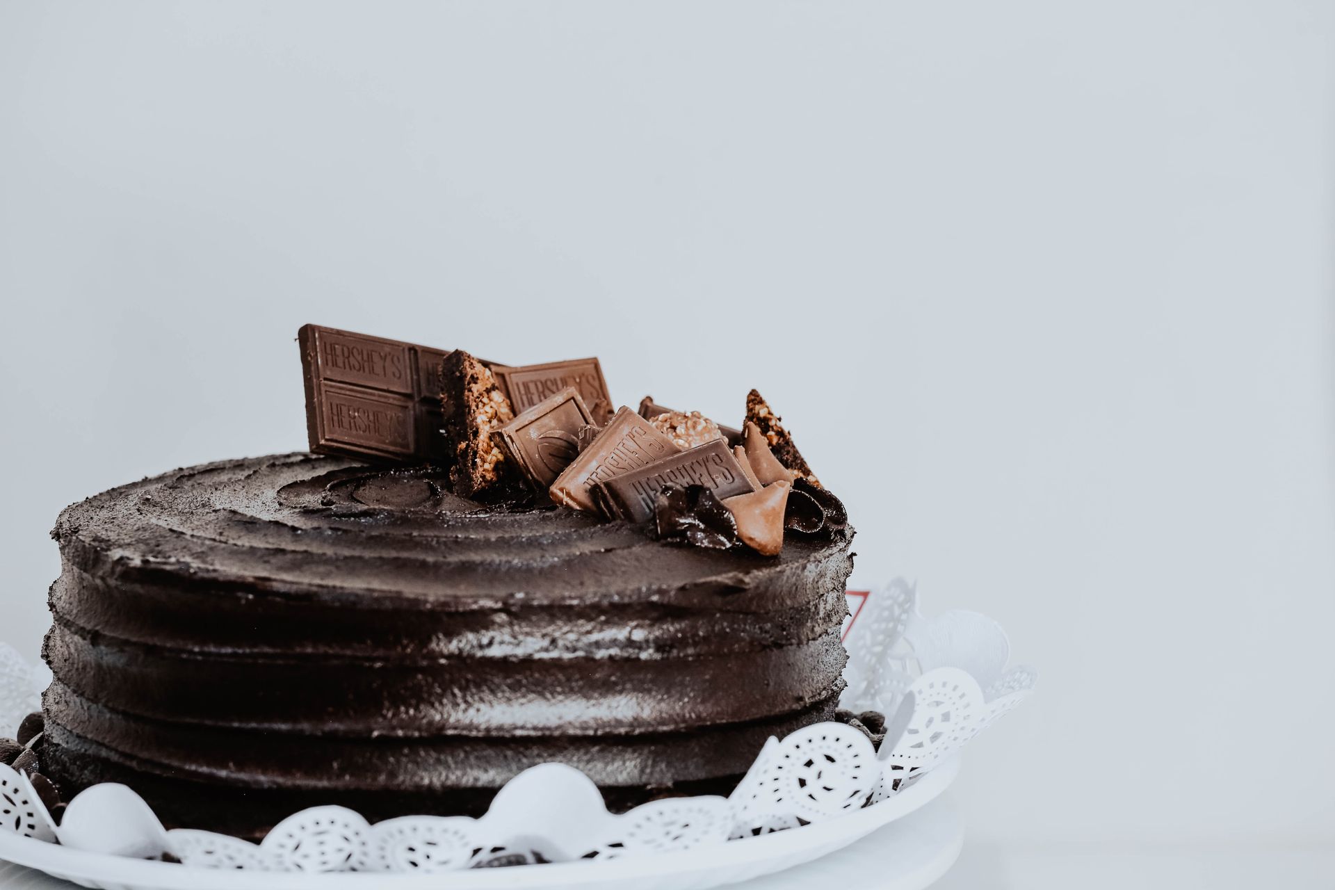 Pastel de chocolate glaseado con trozos de chocolate sobre un plato blanco sobre un fondo claro.