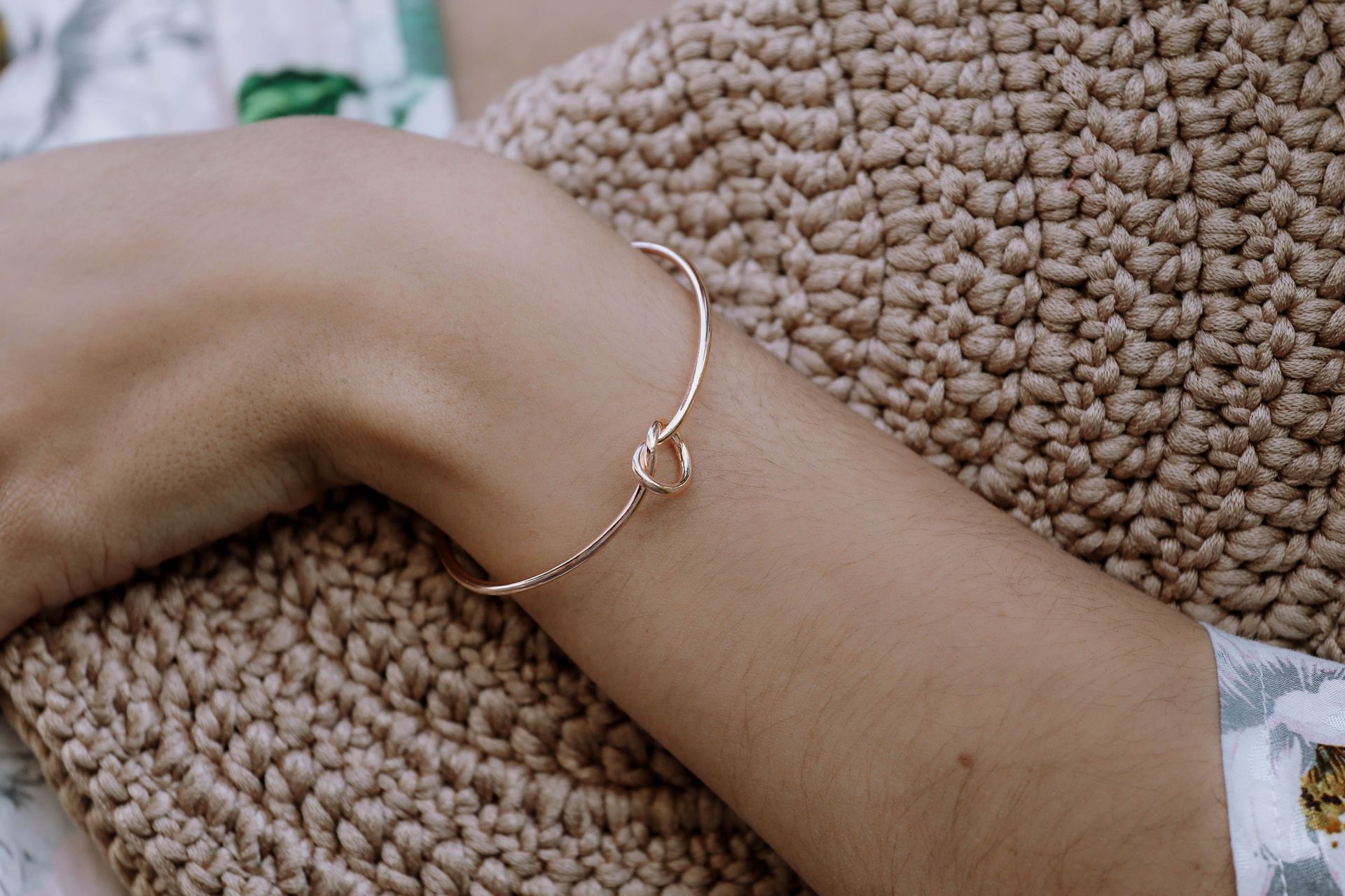 Primer plano de una muñeca con una delicada pulsera de plata sobre una manta de punto color beige.