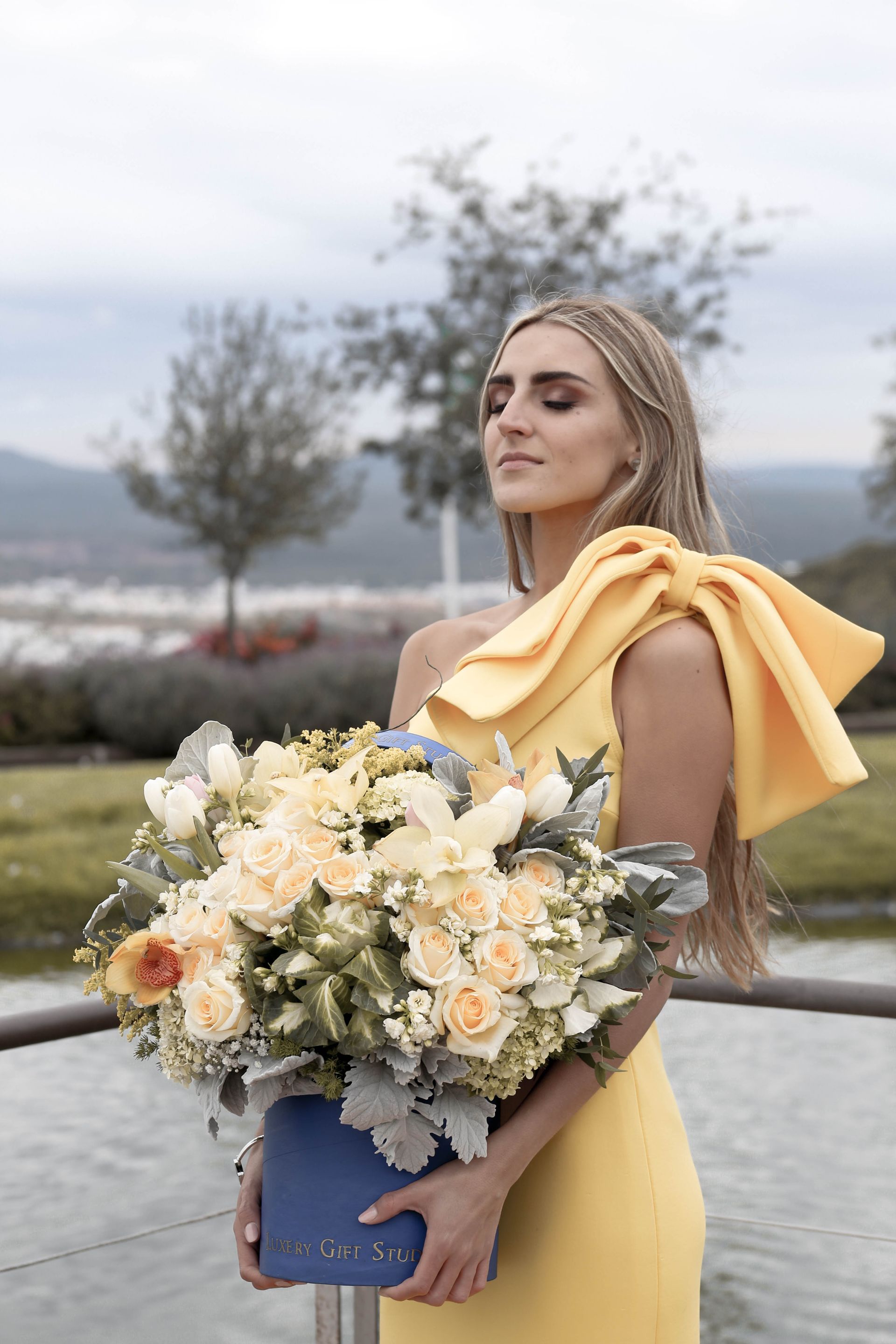 Mujer con un vestido amarillo sosteniendo un ramo de flores al aire libre junto al agua.
