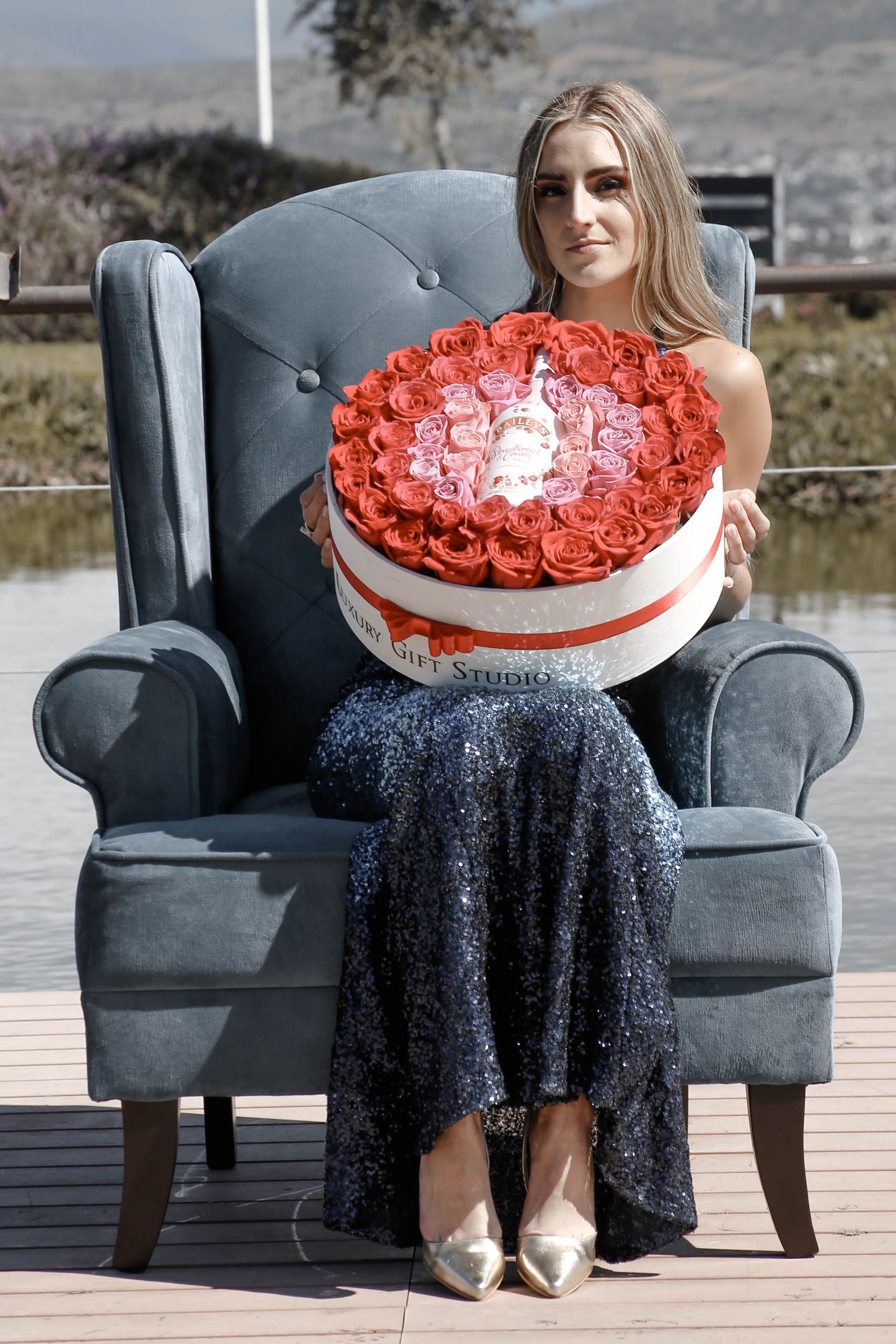Mujer sentada en un sillón azul sosteniendo un gran pastel rojo y blanco al aire libre