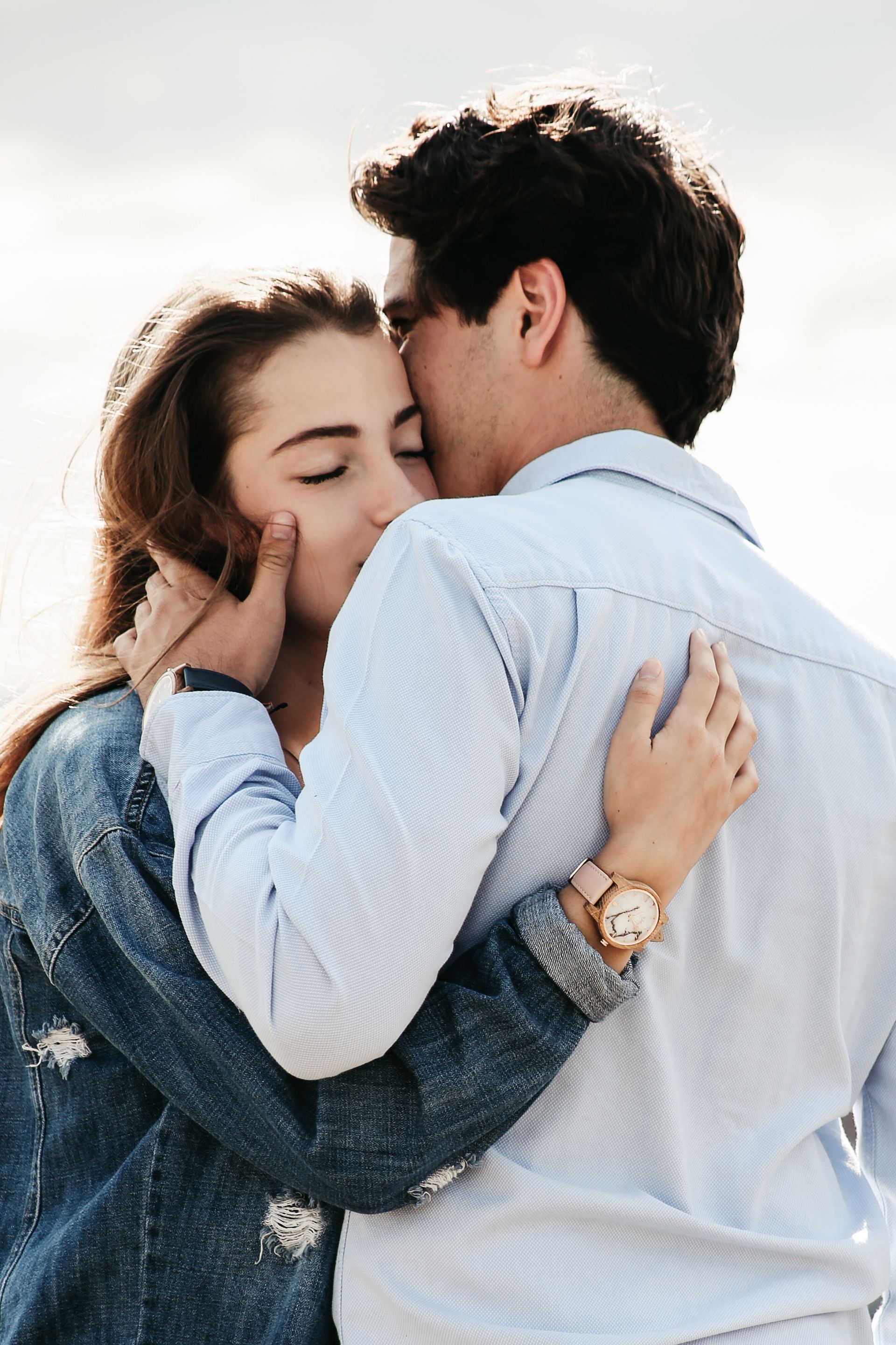 Una pareja se abraza al aire libre, con los ojos cerrados, bajo la suave luz del día.