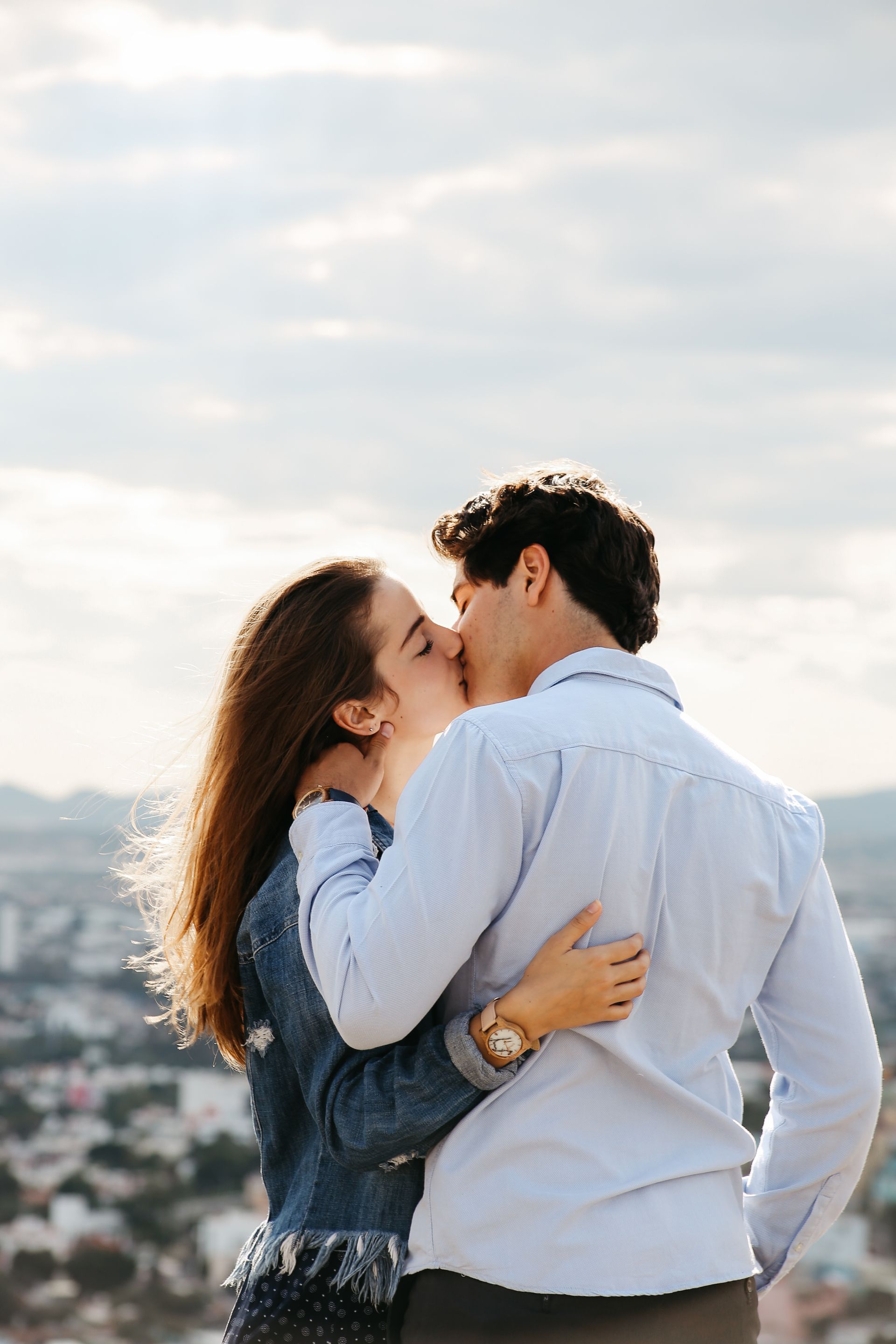 Una pareja se abraza y se besa al aire libre con el horizonte de la ciudad borroso de fondo.