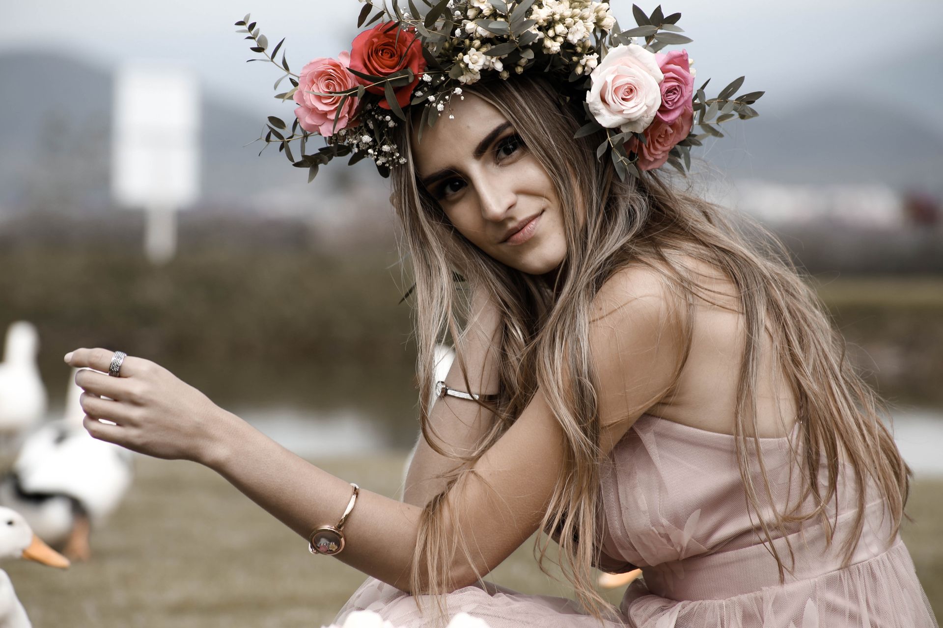 Mujer joven con vestido rosa y corona de flores, sentada al aire libre sosteniendo una taza.