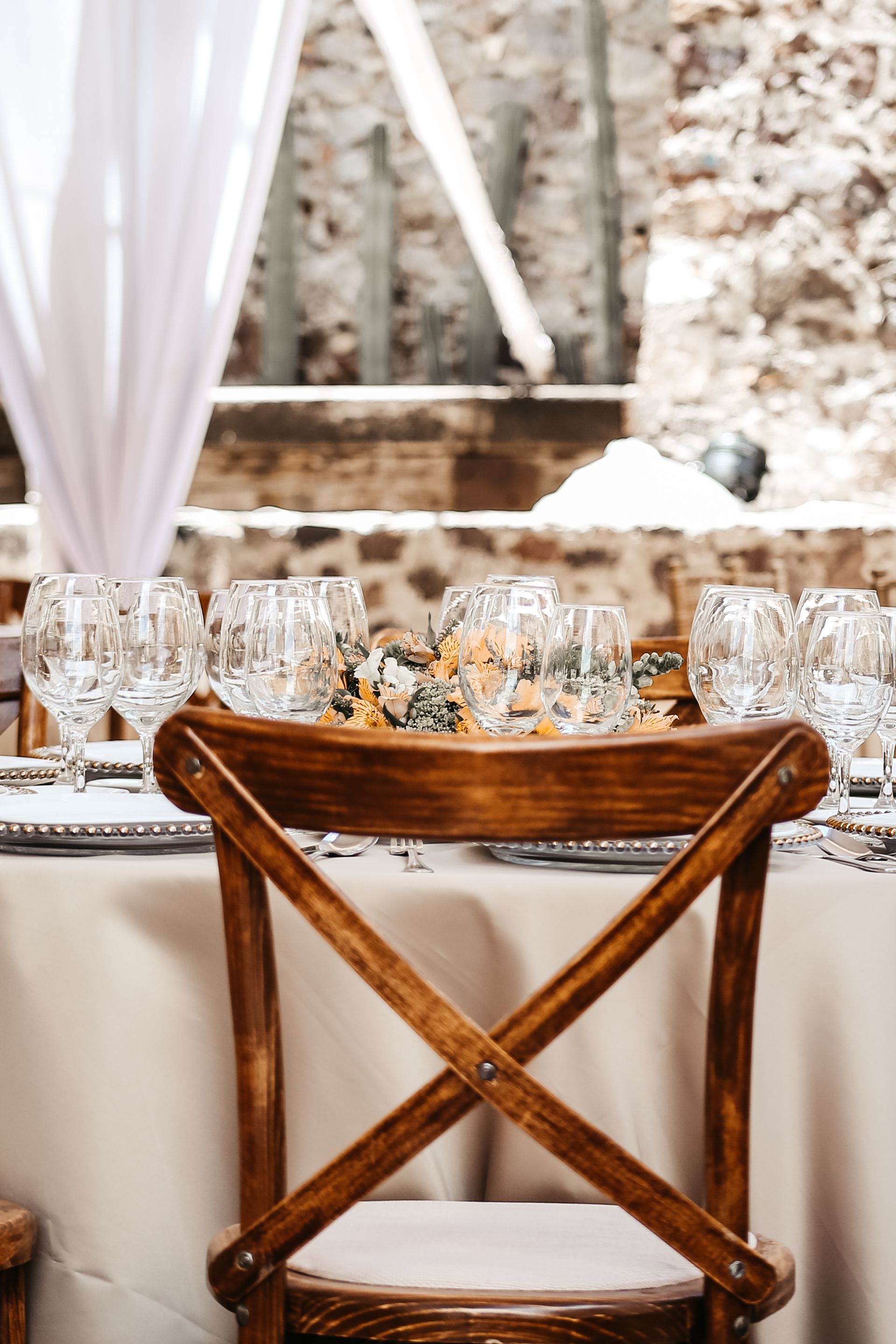 Silla de madera con respaldo cruzado alrededor de una mesa de comedor decorada con cristalería y un mantel blanco.