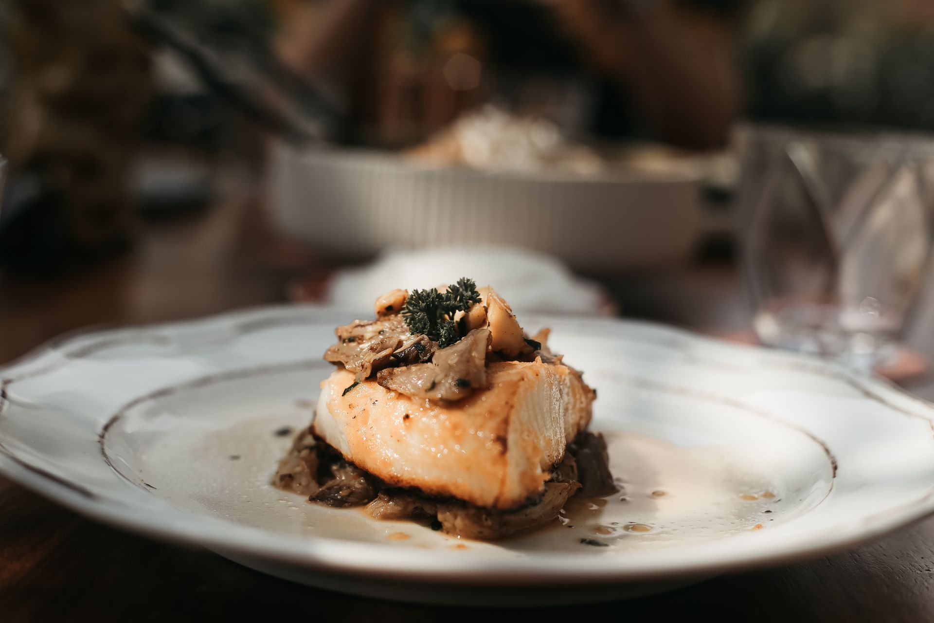 Plato gourmet de pescado con salsa y guarnición servido en una mesa blanca en un restaurante.