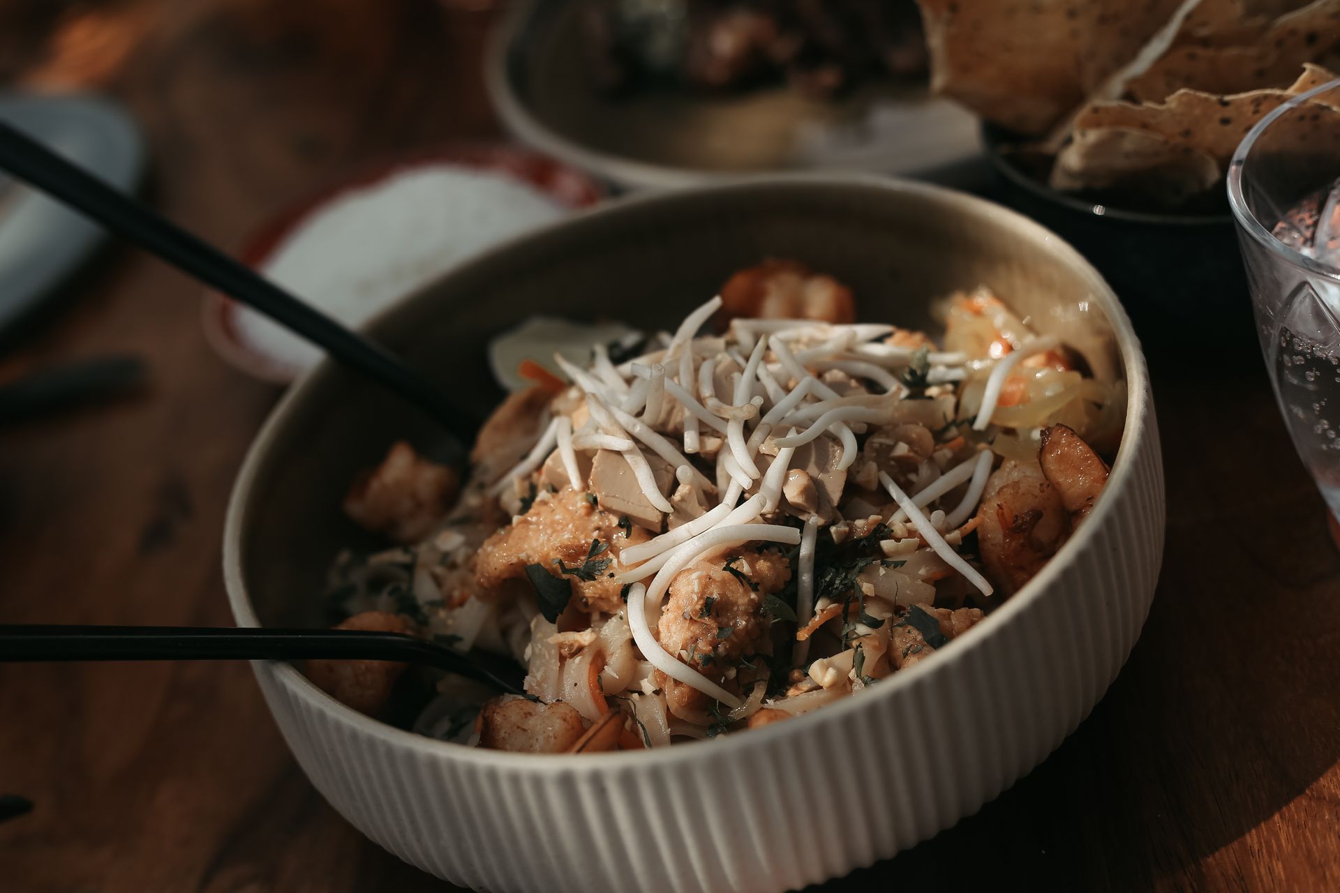Un plato de pasta con queso y hierbas sobre una mesa rústica, con una cuchara cerca.