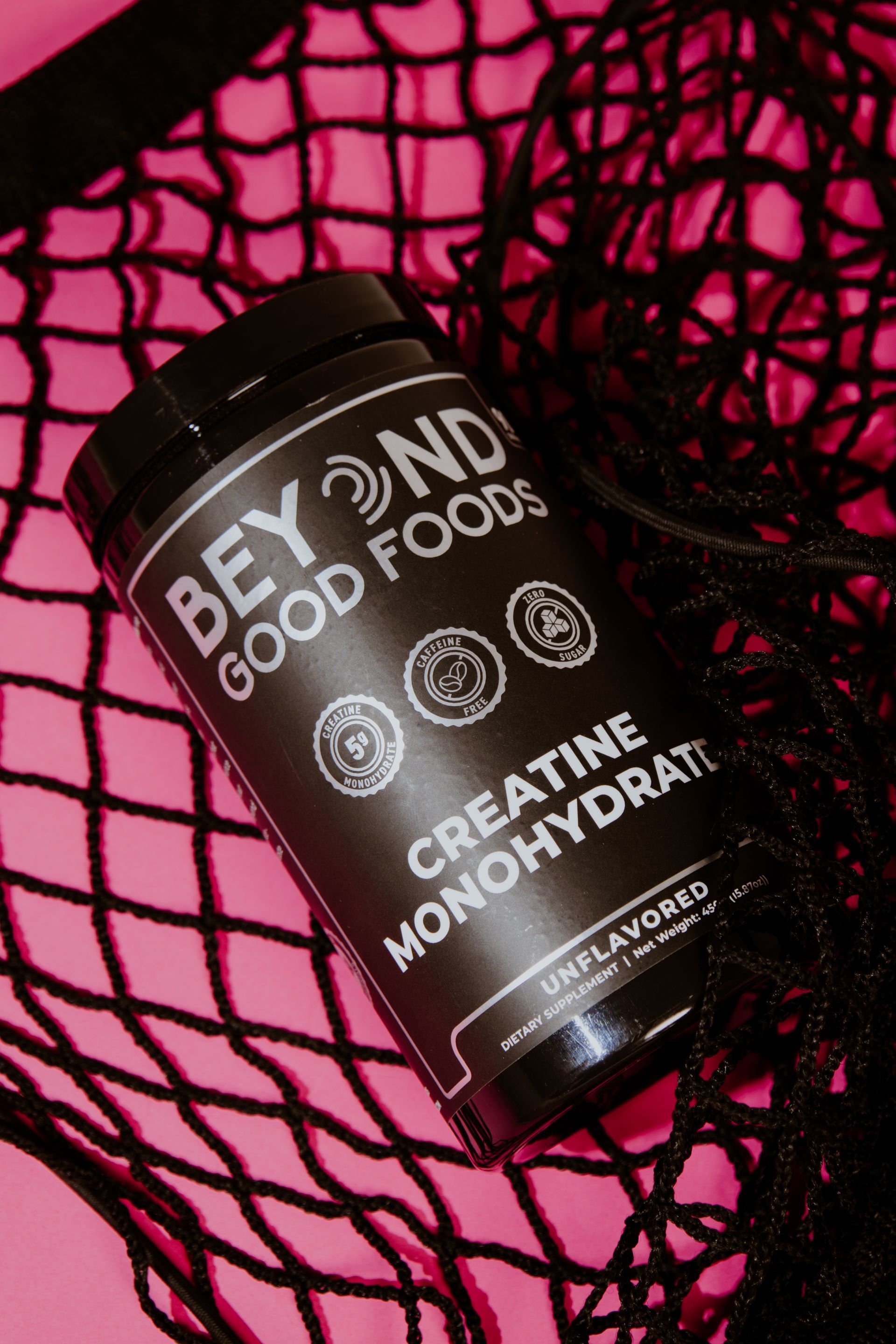 Botella negra de monohidrato de creatina de Beyond Good Foods sobre fondo rosa estampado