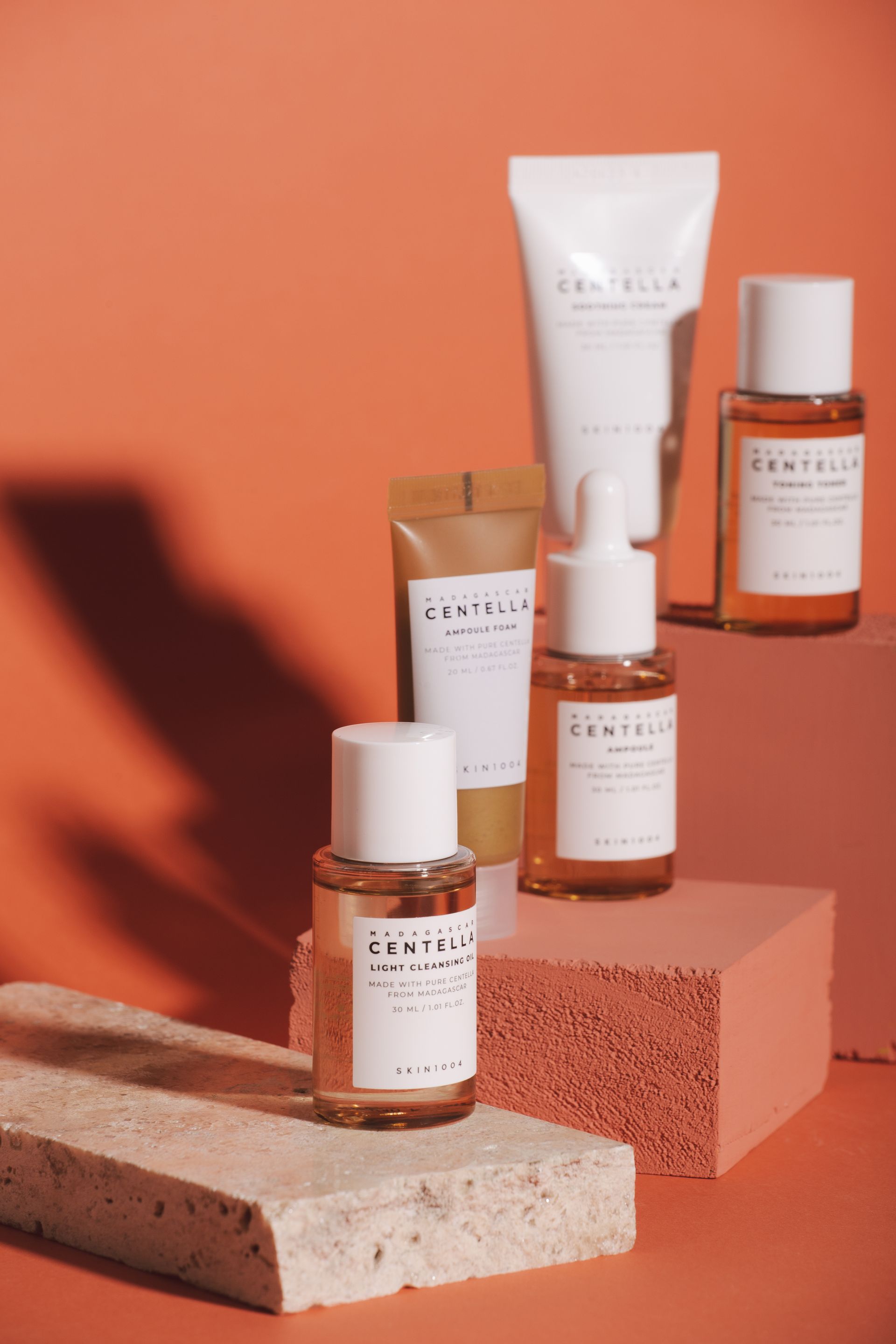 Frascos y tubos de productos para el cuidado de la piel dispuestos sobre bloques de color coral y beige sobre un fondo naranja.